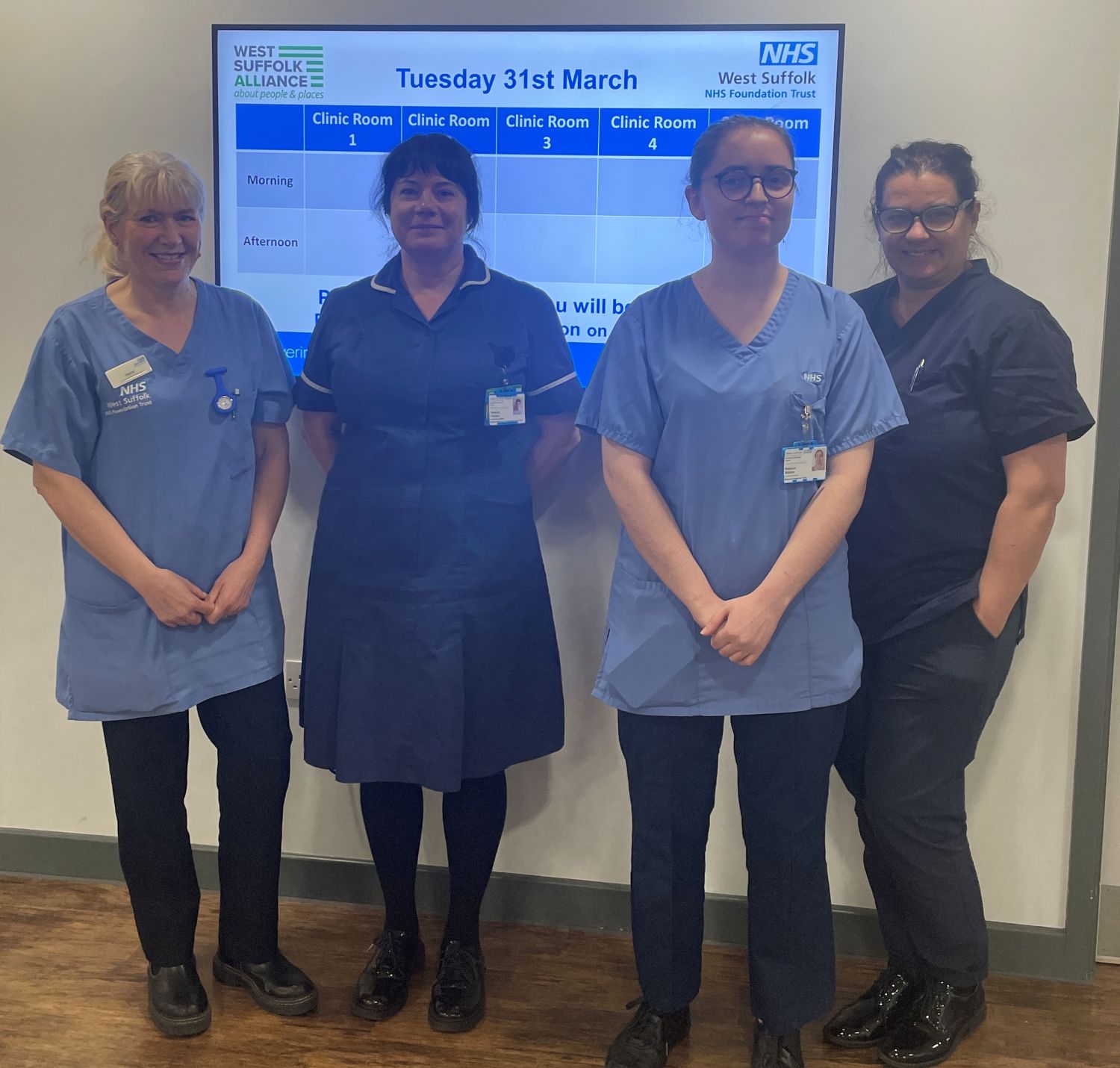 Four team members from WSFT community nursing team, they are standing together and smiling, and are wearing blue scrubs.