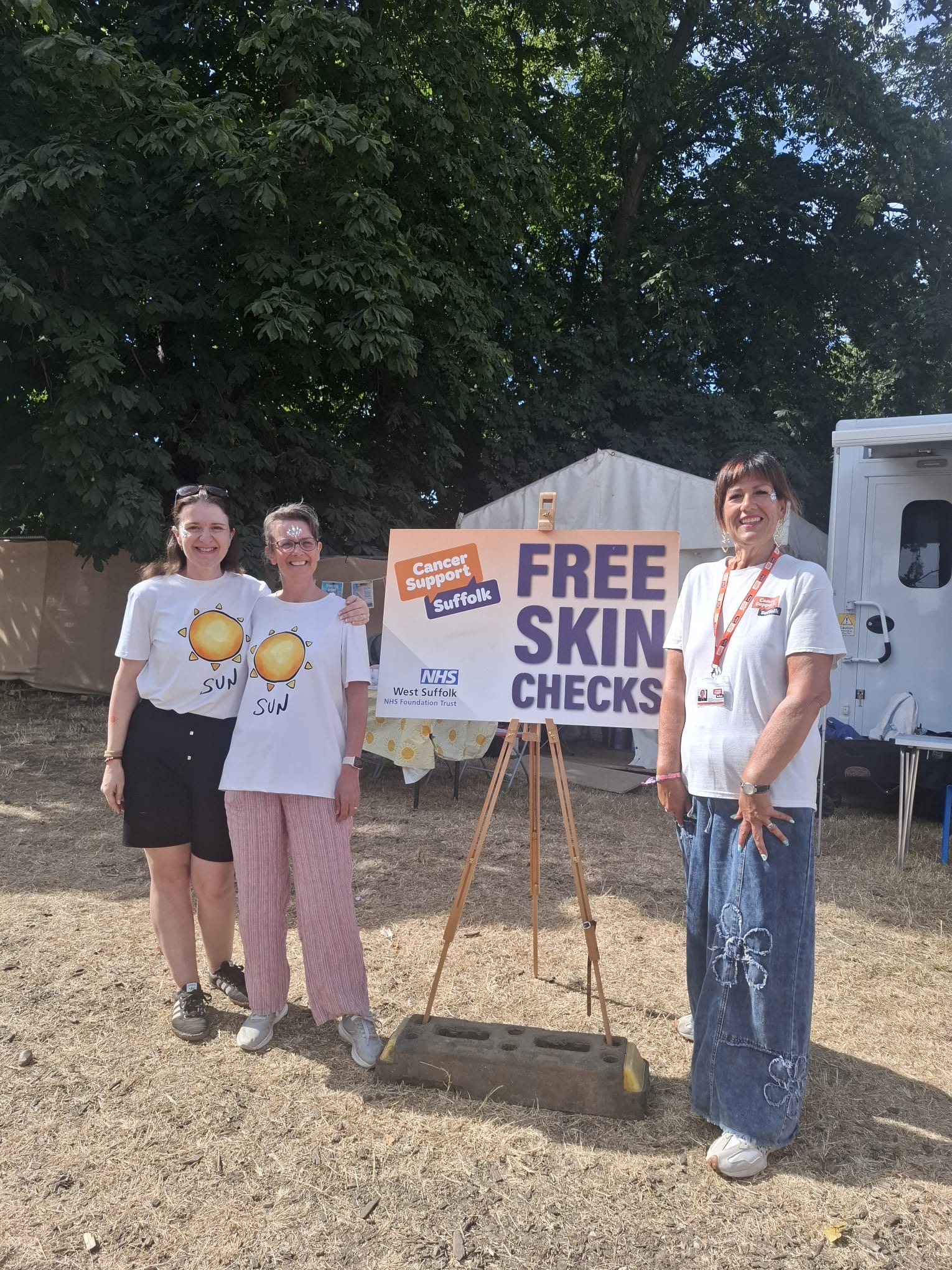 three skin cancer nurses in white shirts stand next to a sign that says 'free skin checks'