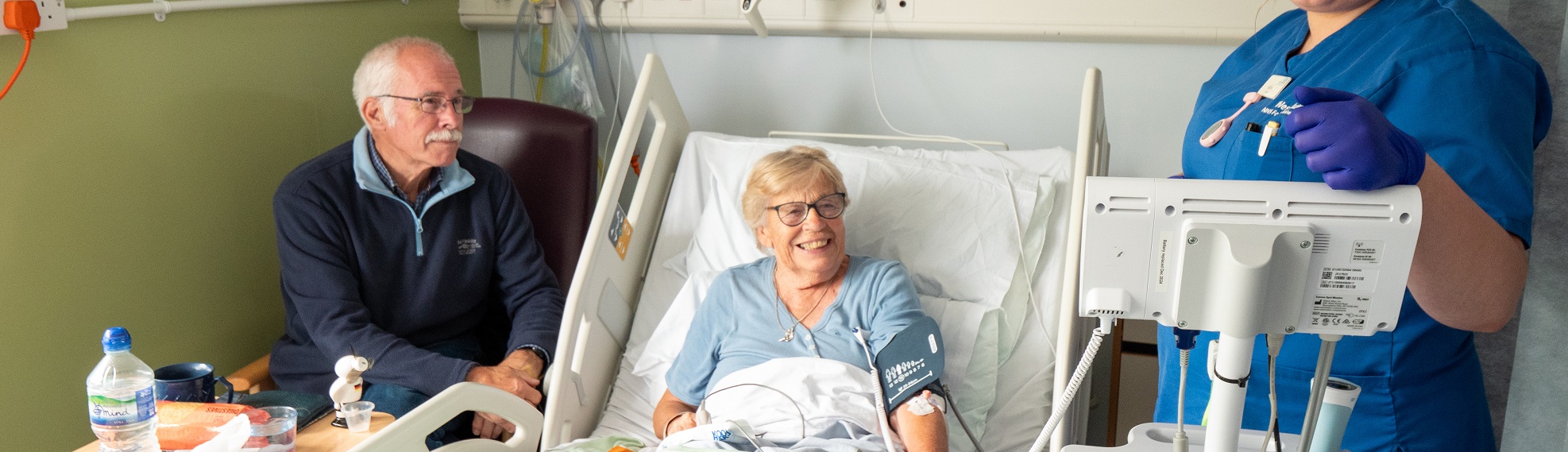 Patient smiling in a hospital bed, with a visitor and nurse at either side