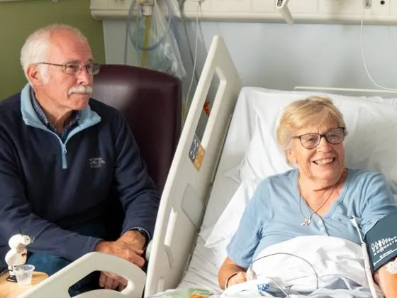 Patient smiling in a hospital bed, with a visitor and nurse at either side