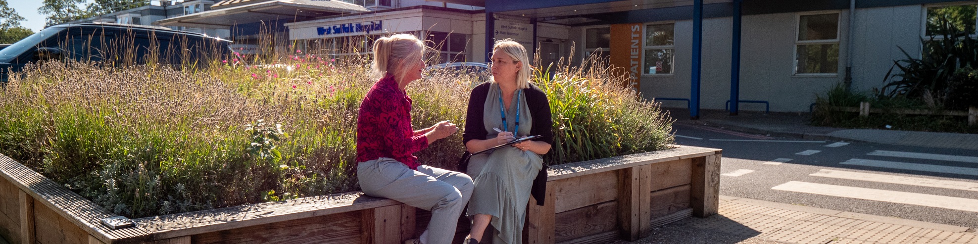Two people chatting on a bench outside West Suffolk Hospital